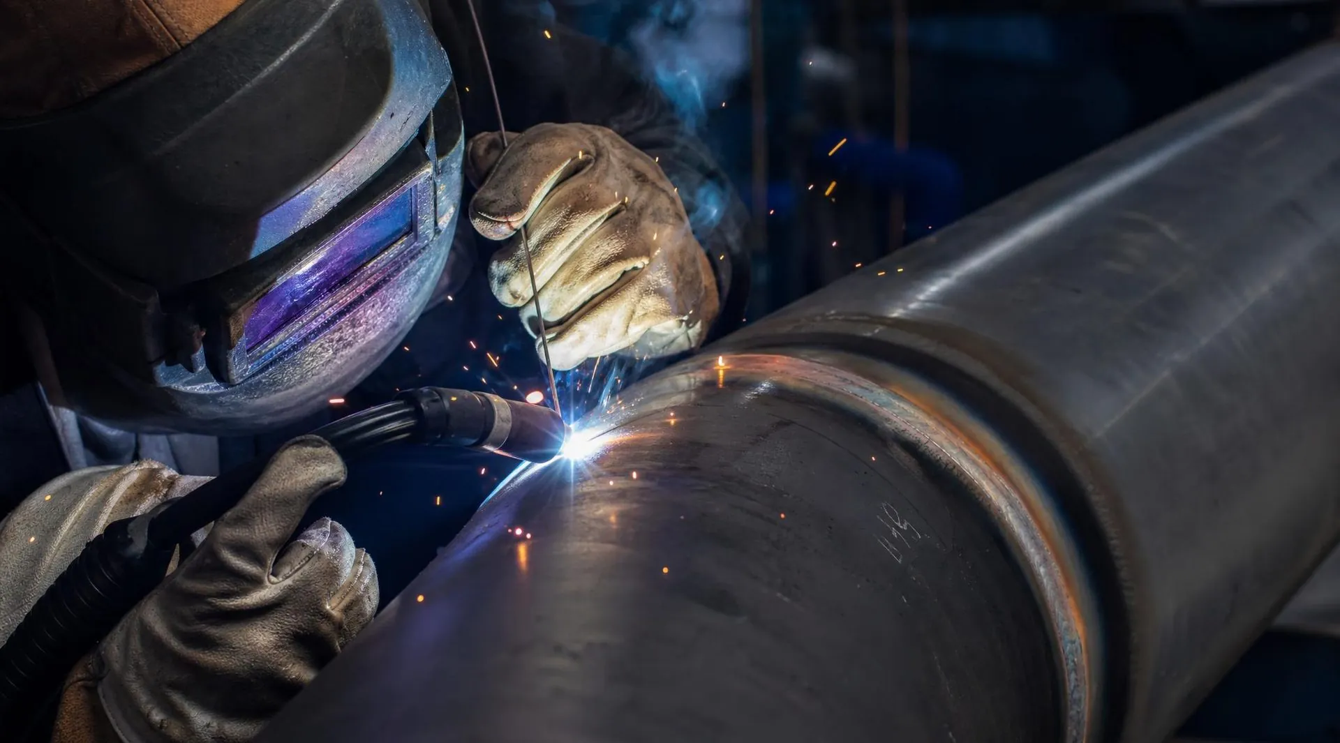 Pipe welder joining large-diameter steel pipe, sparks flying